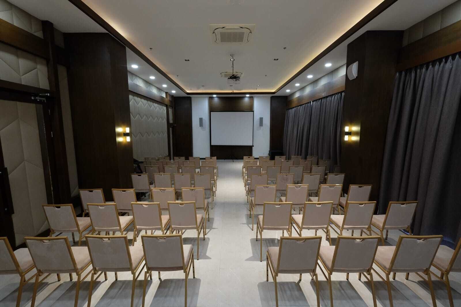 Un salón de conferencias con filas de sillas, una pantalla de proyector y una zona de escenario.