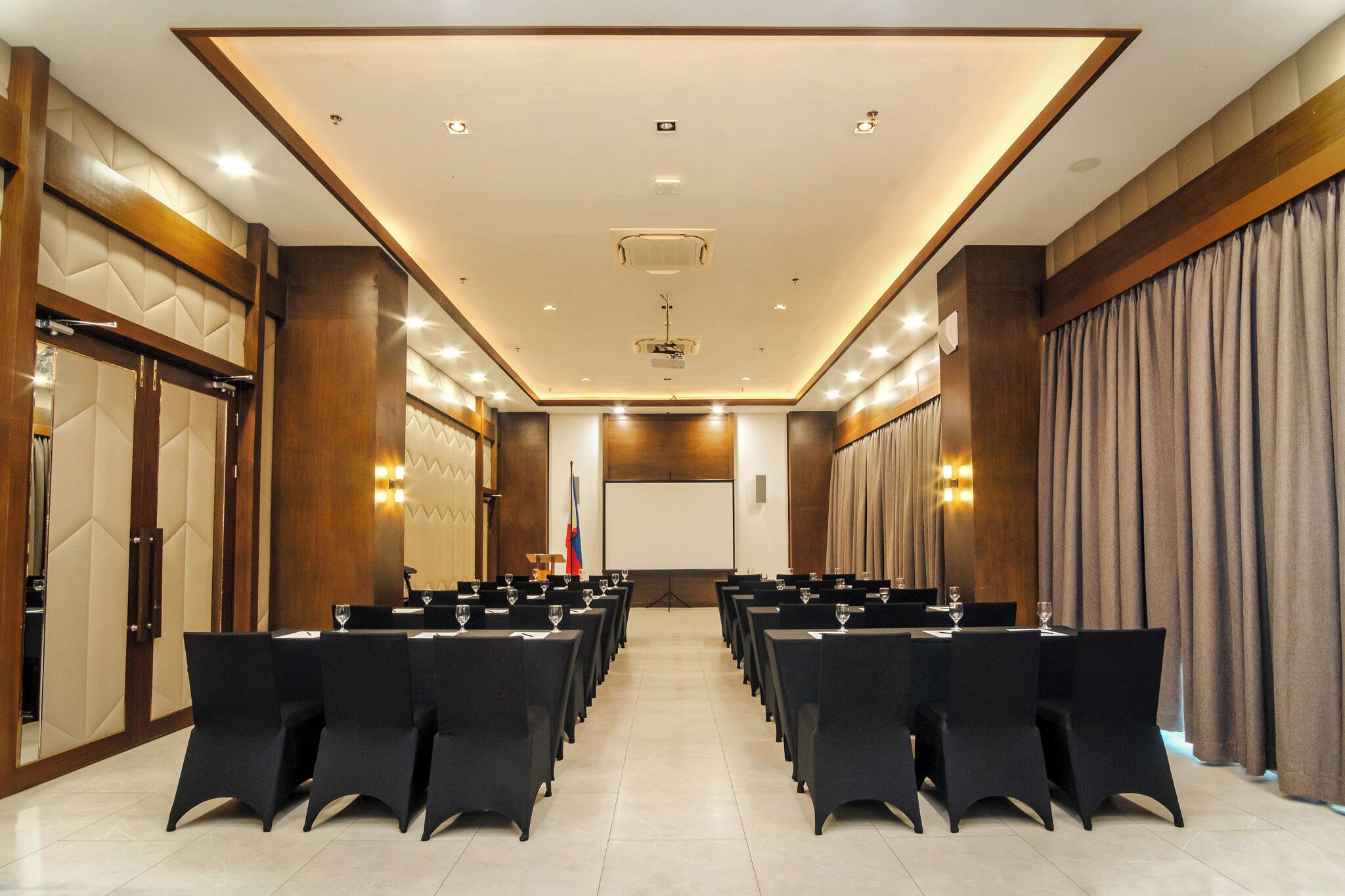 A conference room with rows of tables and chairs, a projector screen, and a flag.