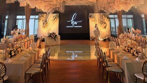 Un salón de bodas con escenario, decoración floral, candelabros y una larga mesa dispuesta para los invitados.
