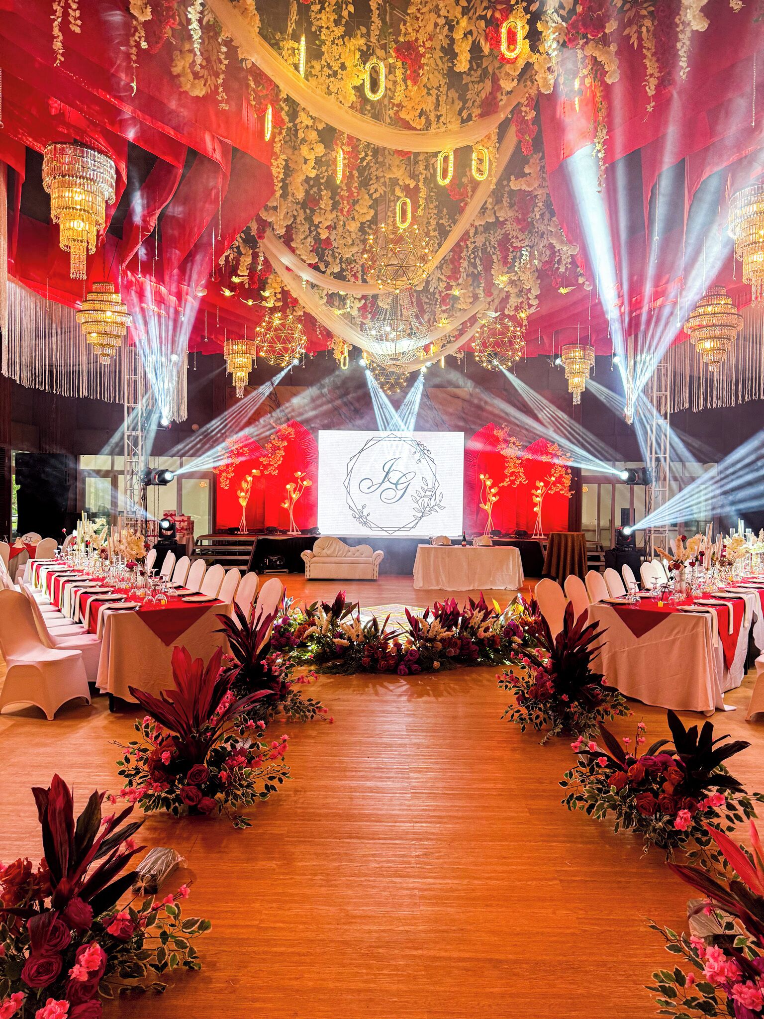 Una sala da banchetti con tavoli apparecchiati per un evento formale, un palco con schermo di proiezione e illuminazione decorativa.