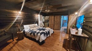 A cozy bedroom with a wooden floor, a bed with a quilt, a nightstand, a desk, and a ceiling fan. - Private, rustic country home with hot tub, movie theater and a view (Pineville)
