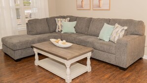A gray sectional sofa with multiple pillows, a wooden coffee table with a bowl of snacks, and a white rug. - Beautiful spacious 4 bedroom house , sleeps 10+ (Raleigh)