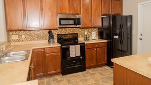 A kitchen with wooden cabinets, a stainless steel microwave, a black stove, a black refrigerator, and a tiled backsplash. - Beautiful spacious 4 bedroom house , sleeps 10+ (Raleigh)