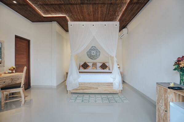 A bedroom with a canopy bed, a wooden desk with a chair, and a decorative wall piece. - Sitala Suite (Ubud)