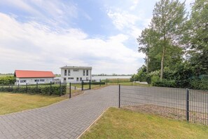 A paved pathway leading to a white building with a red roof, surrounded by greenery and a fence.