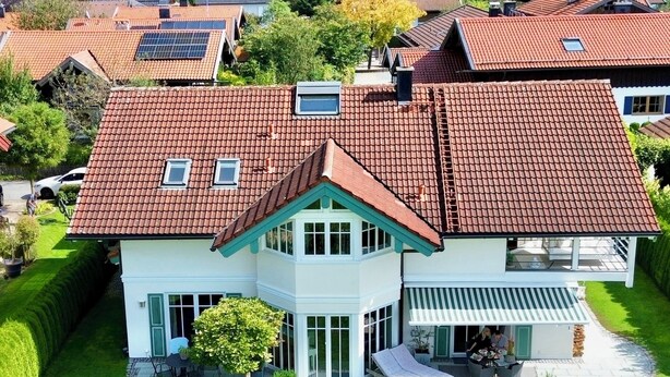 Une grande maison avec un toit recouvert de tuiles rouges, de nombreuses fenêtres et une pelouse bien entretenue.