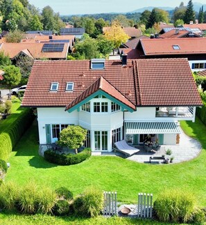 Une grande maison avec un toit recouvert de tuiles rouges, de nombreuses fenêtres et une pelouse bien entretenue.