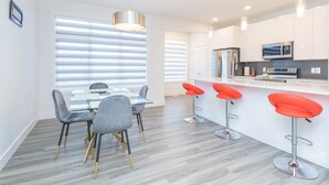 A modern kitchen with white cabinets, stainless steel appliances, and a bar area with red bar stools. - Luxury and Comfort Combined. (Edmonton)