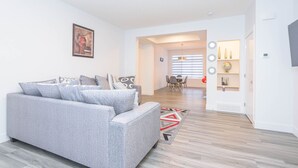 A modern living room with a grey sofa, a dining area with a table and chairs, and a hallway leading to a kitchen. - Luxury and Comfort Combined. (Edmonton)