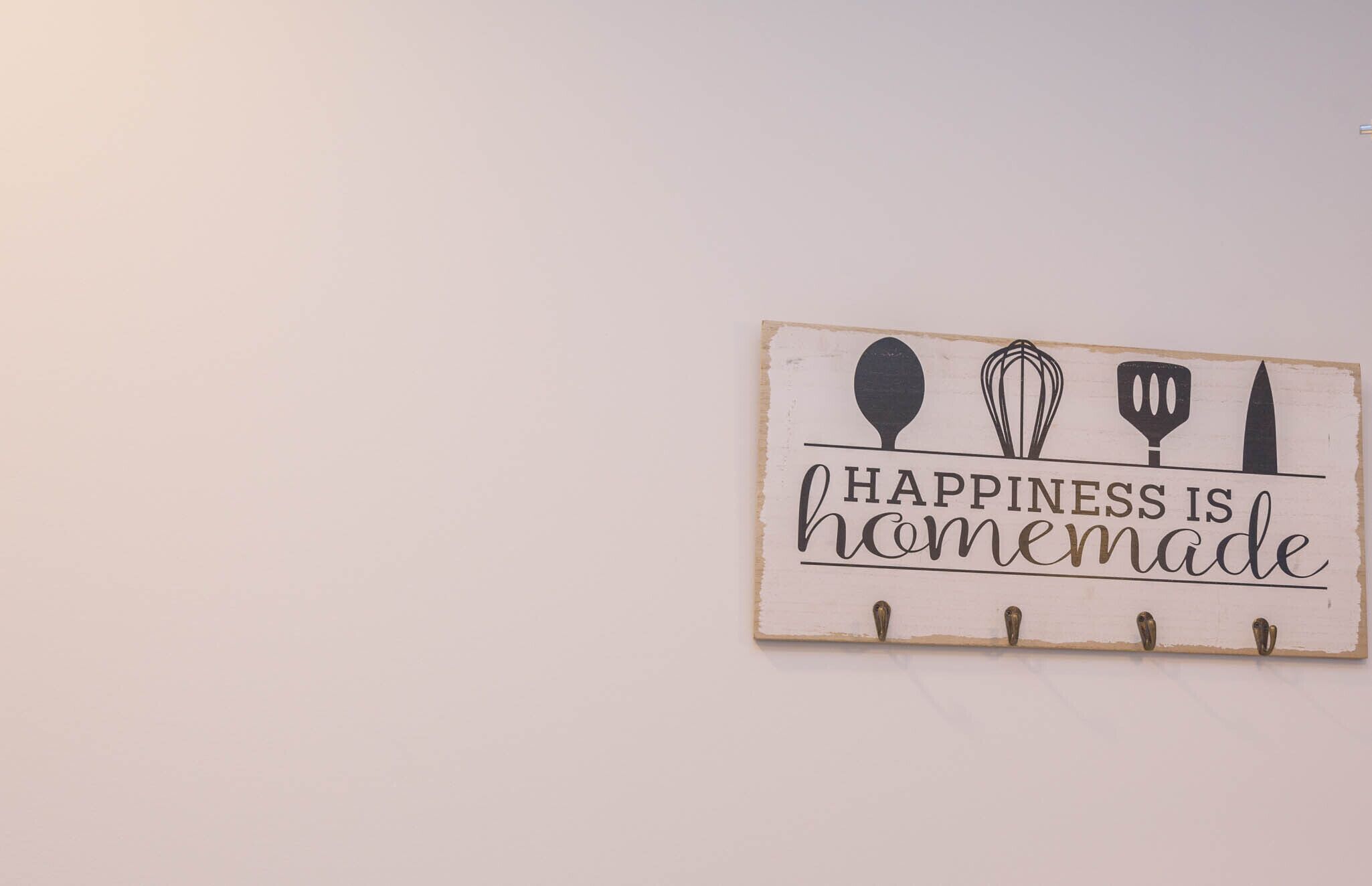 A wall-mounted sign with kitchen utensils and the text "HAPPINESS IS homemade".