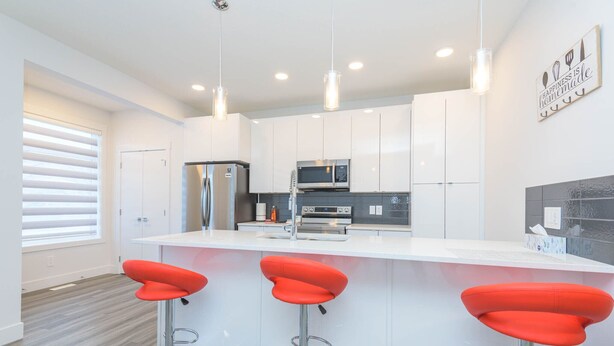 A modern kitchen with white cabinets, stainless steel appliances, and red bar stools. - Luxury and Comfort Combined. (Edmonton)