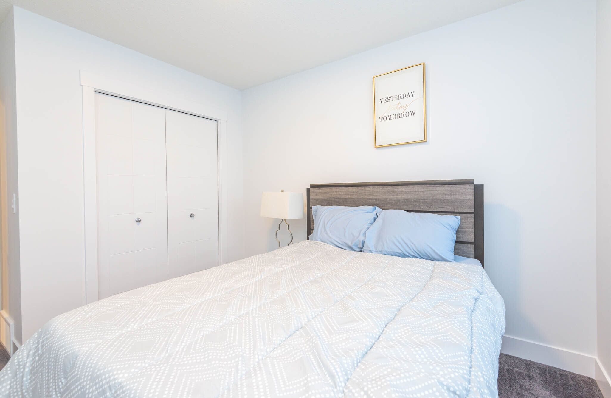 A bedroom with a bed, a nightstand, a wall-mounted lamp, and a framed quote on the wall.