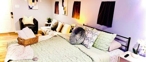 A bedroom with a bed, bedside table, nightstand, and a chair.