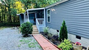 A two-story mobile home with a covered porch, a gravel driveway, and a landscaped garden with various plants and a flower pot.