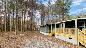 A cabin with a gravel driveway and a wooden deck, surrounded by trees.