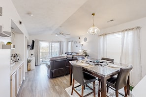 A modern living room with a dining area, a ceiling fan, and a chandelier.