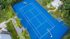 Vista aérea de uma quadra de tênis cercada por vegetação exuberante e área residencial.