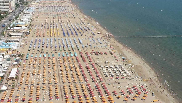 An aerial view of a beach with rows of umbrellas and beach chairs, a promenade, and a clear view of the sea. - Hotel Orizzonti (Rimini)