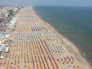 Vista aérea de una playa con hileras de sombrillas y sillas, un paseo marítimo y una vista despejada del mar.