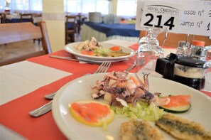 A dining table with plates of seafood, a number sign, and condiments. - Hotel Orizzonti (Rimini)
