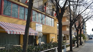 A hotel with a striped awning, outdoor seating, and a sign indicating a pool. - Hotel Orizzonti (Rimini)