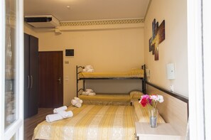 A hotel room with a bunk bed, a wooden wardrobe, a bedside table with a vase of flowers, and a wall-mounted air conditioner. - Hotel Orizzonti (Rimini)