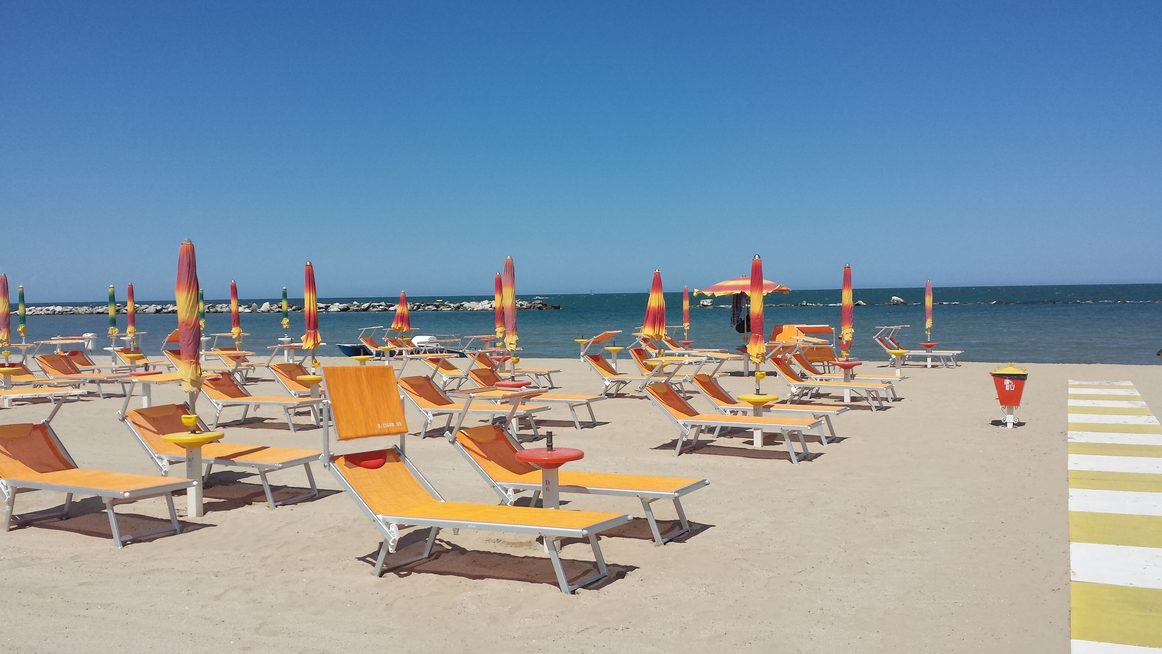 A beach with rows of sun loungers and umbrellas, a clear sky, and the sea in the background.
