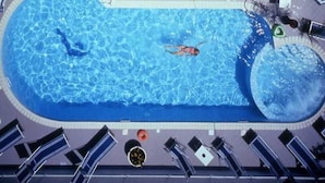 An aerial view of a swimming pool with a person swimming, surrounded by lounge chairs and umbrellas. - Hotel Orizzonti (Rimini)