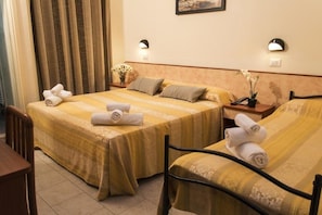 Two single beds with yellow bedspreads and white towels, set against a classic design with wooden headboards and dark metal frames.