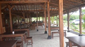 Un restaurant en plein air avec des tables et des chaises en bois, un sol carrelé et une vue sur la verdure environnante.