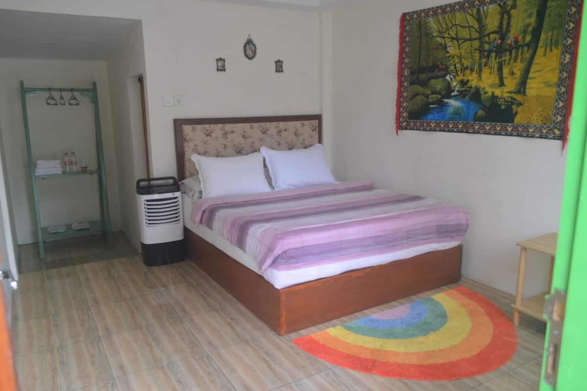 Une chambre à coucher avec un lit, une table de chevet, un radiateur, une étagère avec des serviettes et un tableau encadré au mur.