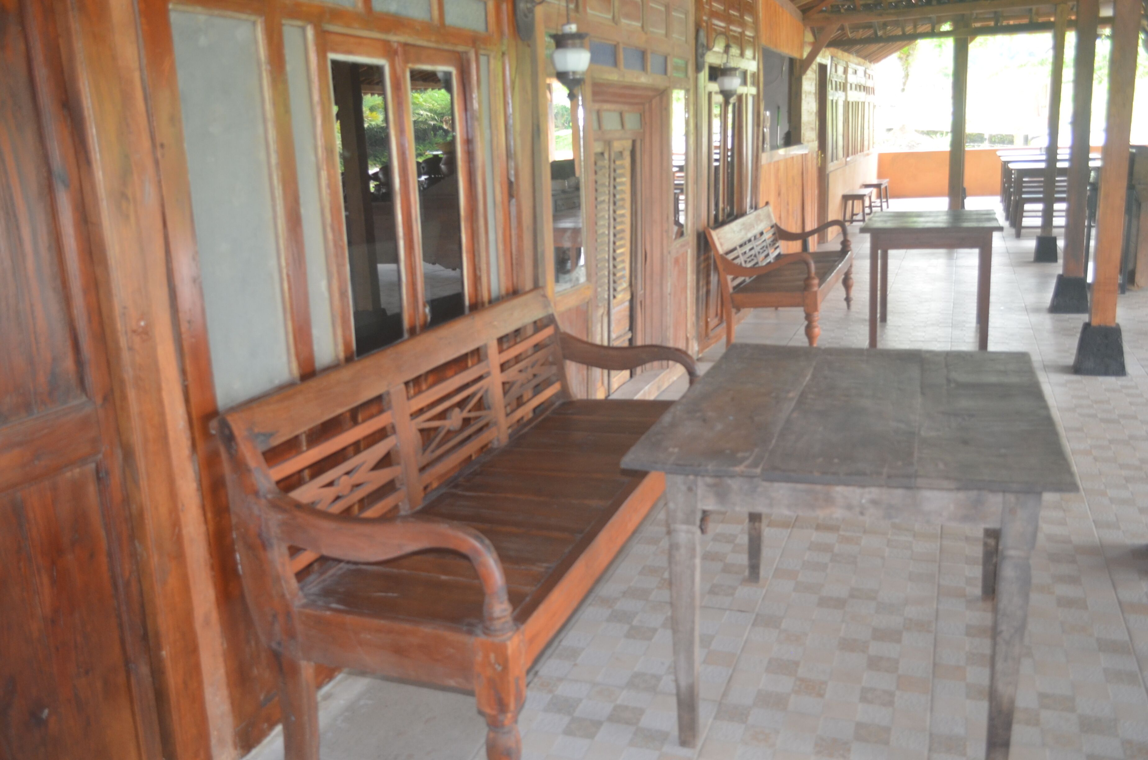 A wooden bench and table in a covered outdoor area with tiled flooring.