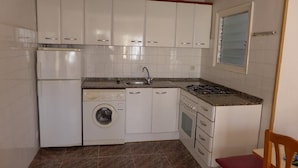 A compact kitchen with white cabinets, a washing machine, a sink, and a stove. - Cye 5 Rentalmar (Vila-Seca)