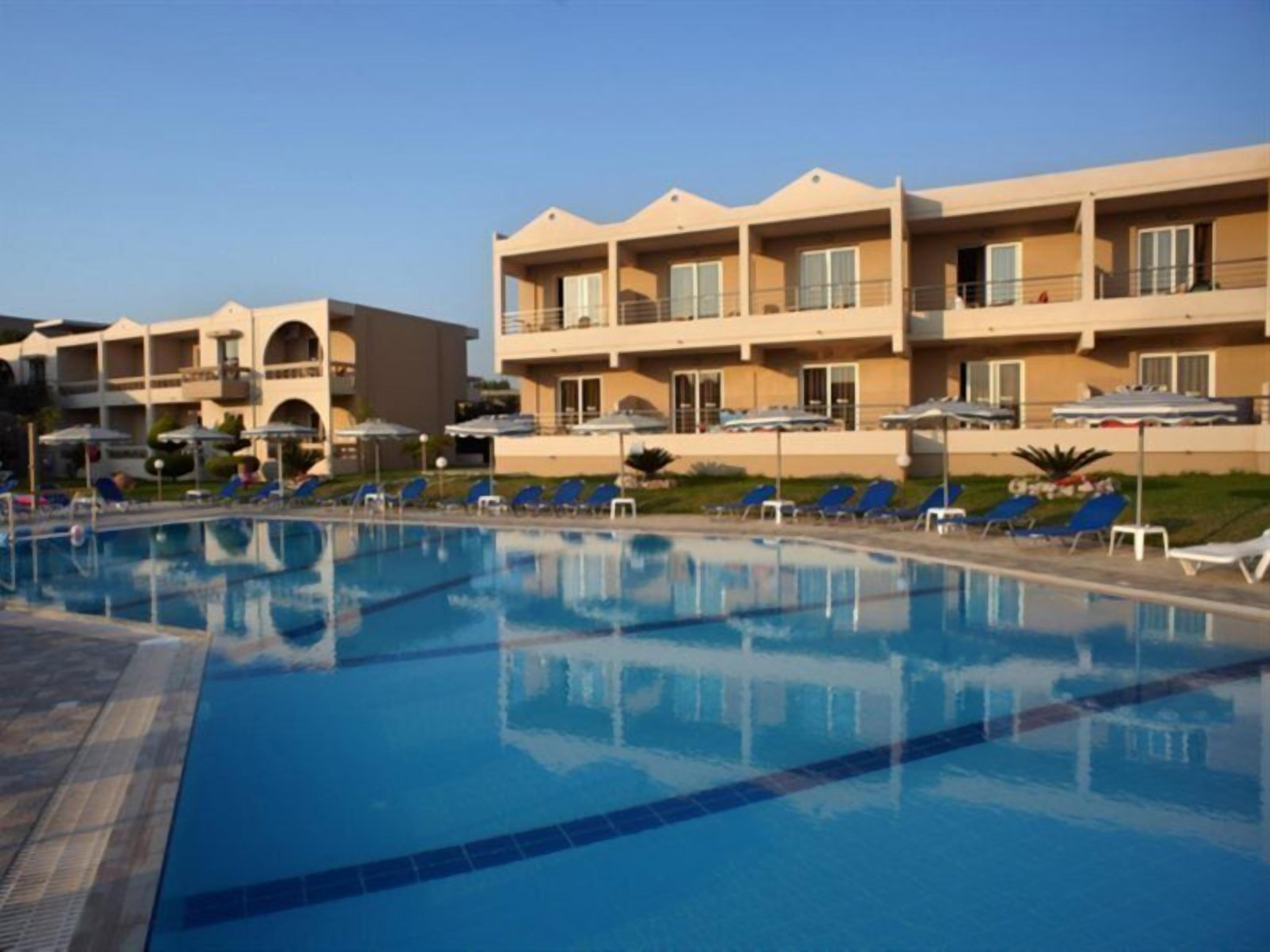 A swimming pool with lounge chairs and umbrellas, surrounded by multi-story hotel buildings with balconies.