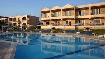 A swimming pool with lounge chairs and umbrellas, surrounded by multi-story hotel buildings with balconies.