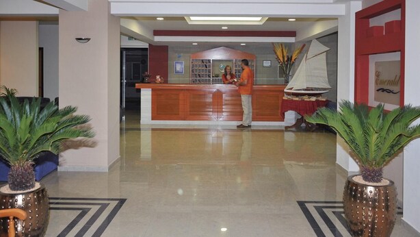 A reception area with a wooden counter, a large potted plant, and a decorative sailboat. - Emerald Apartments (Rhodes)