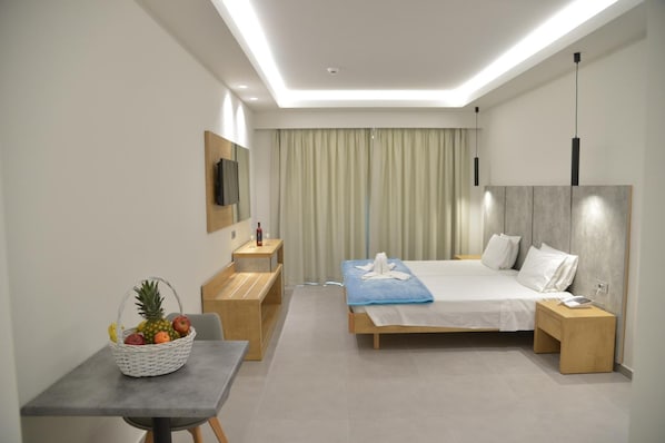 Habitación de hotel moderna con cama, mesitas de noche, escritorio, silla, televisor y frutera.