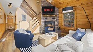 En hyggelig stue med en pejs af sten, et Netflix skilt, trægulv og en trappe.