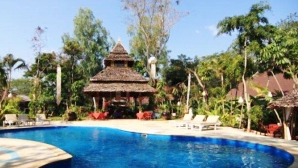 Una piscina con una estructura de techo de paja al fondo, rodeada de exuberante vegetación.
