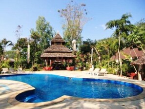 A swimming pool with a thatched-roof structure in the background, surrounded by lush greenery. - Mae Hong Son Mountain Inn and Resort (Mae Hong Son)