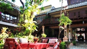 Un patio con una mesa y sillas rojas, rodeado de vegetación exuberante y arquitectura tradicional.
