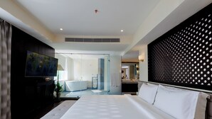 Una habitación de hotel moderna con una cama grande, televisor, baño con bañera y un adorno de pared.