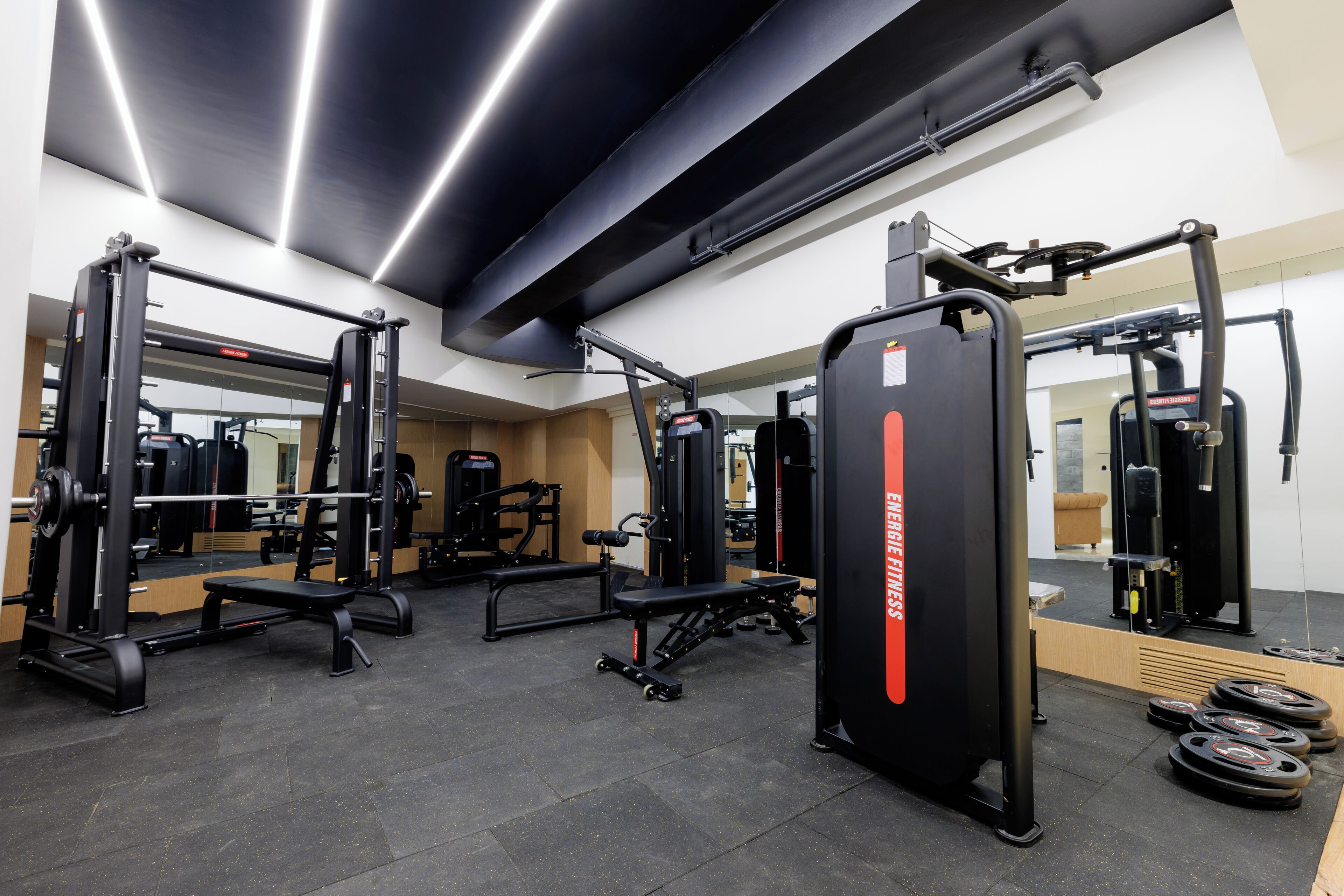 Un gimnasio con equipo de levantamiento de pesas, bancos y un espejo.