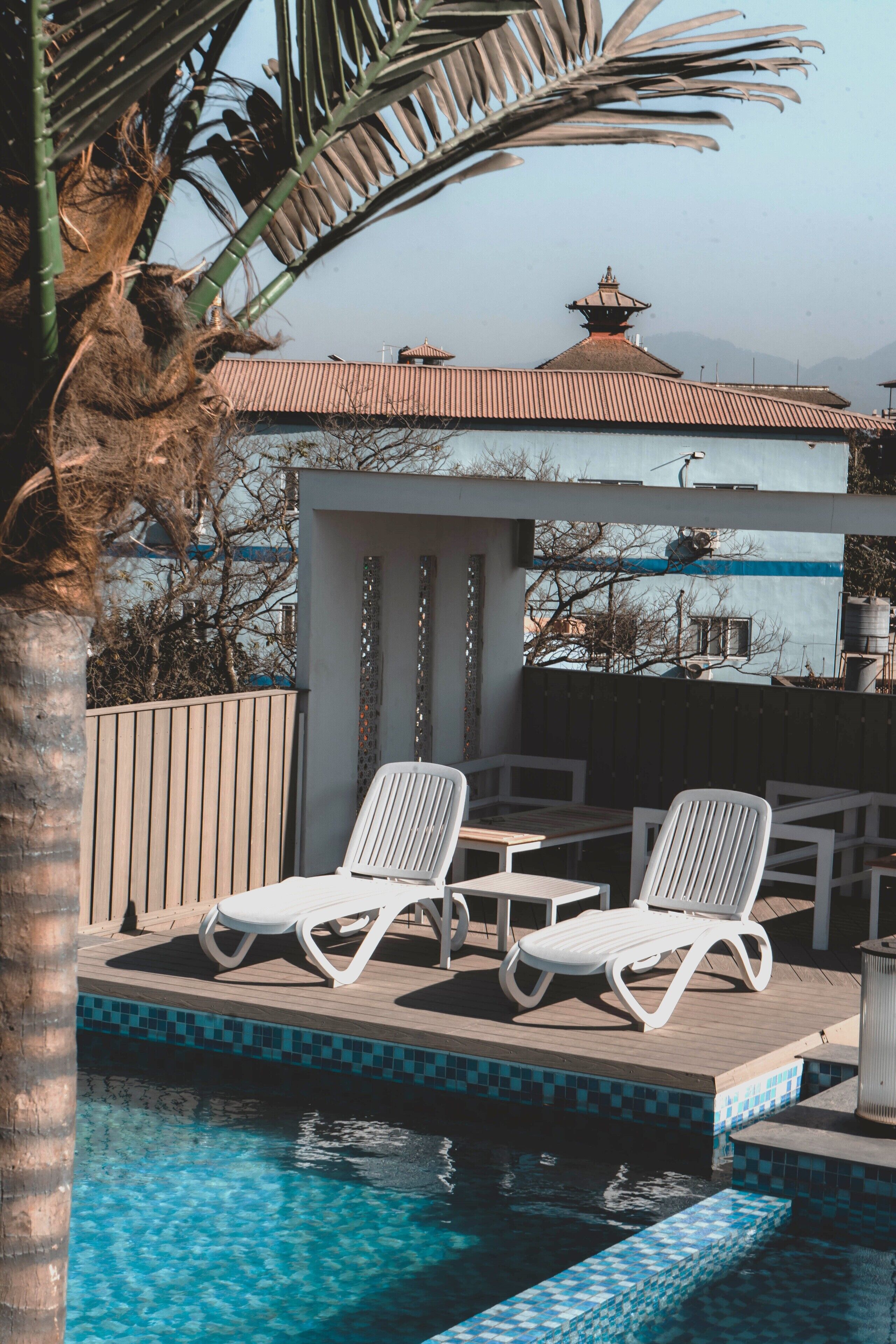 Zona de piscina con dos sillas reclinables blancas, una mesita y una piscina con azulejos.