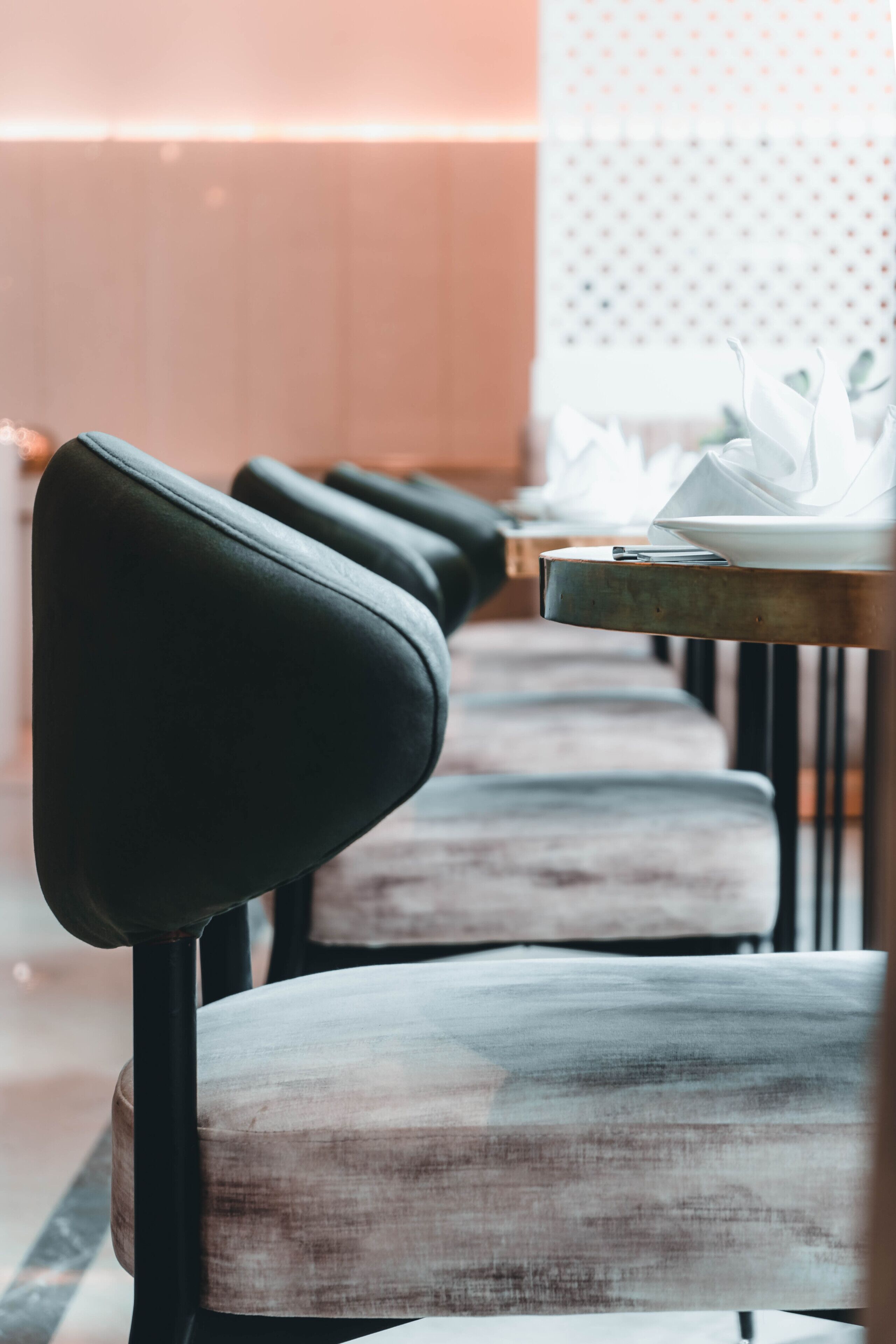 A row of modern chairs with a metal frame and cushioned seats, arranged in a dining area with a patterned wall and a table with a white napkin and a plate.