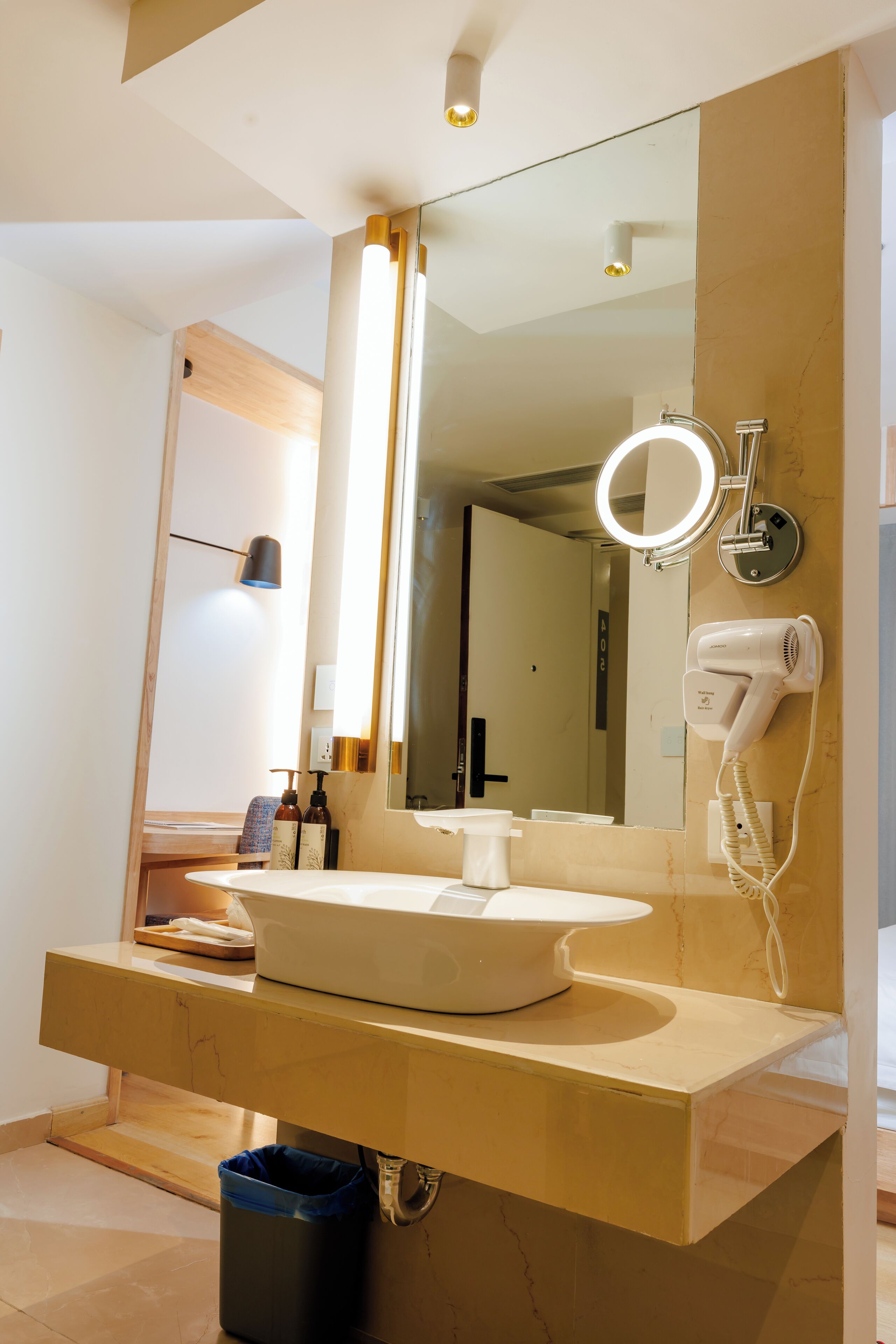 A modern bathroom with a large mirror, a round vanity, a hairdryer, and a trash bin.