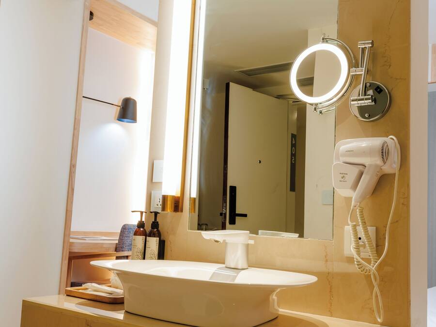 A modern bathroom with a large mirror, a round vanity, a hairdryer, and a trash bin.