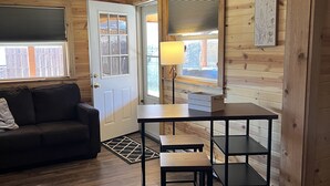 Une pièce chaleureuse avec un plafond en bois, un canapé, une table avec des chaises et une fenêtre avec des stores.