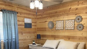 Une chambre aux murs lambrissés, avec un lit, un ventilateur de plafond et des œuvres d’art décoratives.