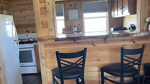 Une cuisine de taille réduite avec des murs en bois, un réfrigérateur, une cuisinière et deux chaises noires.